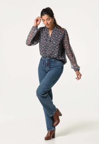 Doorzichtig bloemetjesblouse met lange mouwen, kraag en knoopsluiting, gecombineerd met hoge taille blauwe spijkerbroek en bruine haklaarzen.