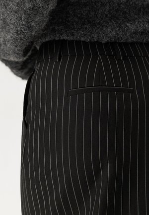 Pantaloni neri a righe sottili realizzati in tessuto intrecciato, con vita piatta, tasche laterali e tasca posteriore con filetto. La texture appare liscia.