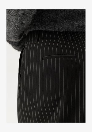 Pantaloni neri a righe sottili realizzati in tessuto intrecciato, con vita piatta, tasche laterali e tasca posteriore con filetto. La texture appare liscia.