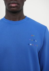 Blauer Sweatshirt mit rundem Halsausschnitt und Rippbündchen. Auffälliger, mehrfarbiger gestickter Text auf der linken Brustseite. Material aus Baumwollmischung.