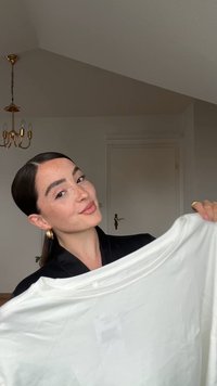 Tricou alb, lejer, din material moale, cu decolteu rotund și mâneci scurte. Modelul îl ține sus, zâmbind.