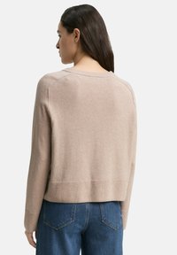 Beige gebreide sweater met een ronde hals en geribbelde onderkant, met raglanmouwen en een zachte textuur, gecombineerd met blauwe spijkerbroek.