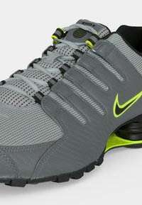 Γκρι και μαύρο αθλητικό παπούτσι Nike Shox με νέον κίτρινα στοιχεία, επάνω μέρος από δίχτυ και ορατή ελαστική απορρόφηση στο πέλμα.
