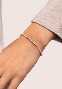 Bracciale di perline al polso, caratterizzato da piccole perle rotonde in colori pastello, intervallate da accenti dorati, design flessibile e forma sottile.