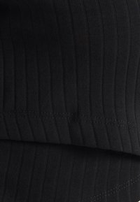 Svart ribbat tyg med vertikala linjer, slät yta och synlig sömdetalj längs fållen. Mjukt och elastiskt material.