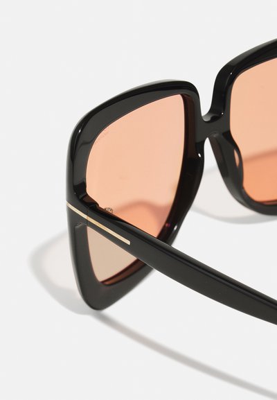 Μαύρα γυαλιά ηλίου με γωνιώδη σκελετό, πορτοκαλί φακούς και χρυσά αξεσουάρ στους βραχίονες. Διαθέτουν γυαλιστερή φινιρίσματος και έντονο γεωμετρικό σχέδιο.