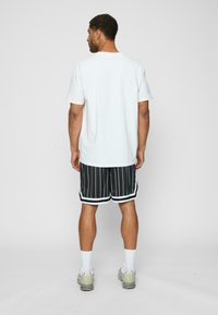 Tricou alb cu mânecă scurtă, cu o croială lejeră, purtat cu pantaloni scurți negri cu dungi fine și accente albe, completat cu adidași atletici ușori.