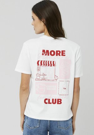 T-shirt en coton blanc avec un design graphique au dos comprenant le texte rouge "PLUS" et "CLUB", ainsi que des illustrations d'un café, d'une tasse de café et d'un croissant.