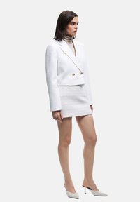 Hvid tweed cropped blazer med dobbelte guldknapper, parret med en matchende tekstureret mini-nederdel og hvide hælede mules.