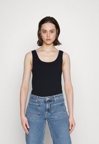 Bodysuit preto sem mangas com decote arredondado, combinado com jeans de ganga azul claro de cintura alta, apresentando bolsos frontais e traseiros.
