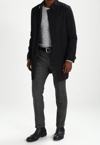 Czarny płaszcz, szary sweter dzianinowy, szare spodnie o fakturze oraz czarne botki. Charakterystyczne detale: płaszcz ma kołnierz, guziki i mankiety.