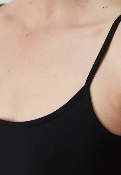 Top sans manches noir avec un col arrondi. Tissu doux et lisse avec des fines bretelles, coupe près du corps, laissant entrevoir le teint de la peau en dessous.