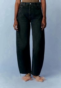 Vaqueros de mezclilla negros de cintura alta con una silueta de pierna ancha, con dobladillos deshilachados y diseño de cinco bolsillos. Combinados con zapatos rosa claro.