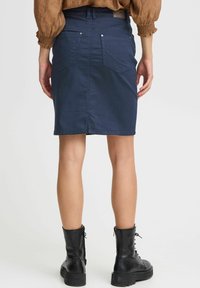 Marinblå denimkjol med en figurnära passform, bakfickor och synliga sömmar. I kombination med svarta snörstövlar.
