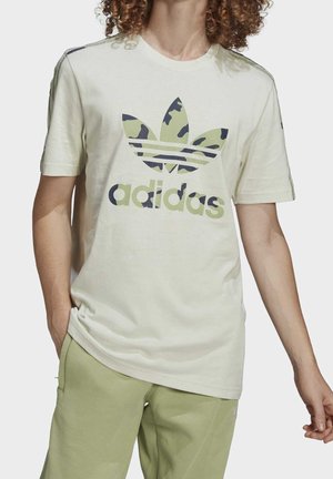 Jasnobeżowa bawełniana koszulka z zielonym i granatowym kamuflażowym logo Adidas, krótkie rękawy, okrągły dekolt i ozdobne paski na ramionach.