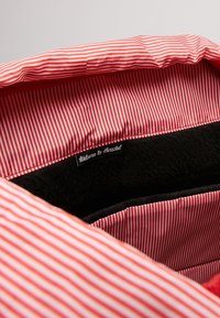 Czerwono-biała podszewka w paski z pluszowym czarnym wnętrzem. Etykieta brzmi "Witamy w Herschel". Miękka faktura i gładkie wykończenie.