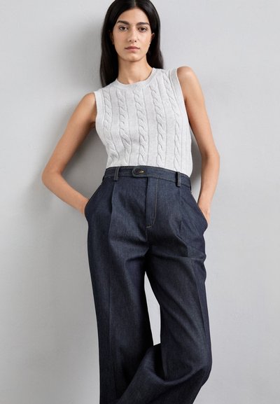 Pull sans manches en tricot gris, associé à un pantalon en jean foncé taille haute avec plis et un accent de bouton.