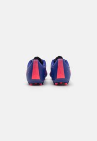 Botas de fútbol azules con un upper texturizado, que presentan acentos rosas en el talón y la parte posterior, y seis tacos rojos en la suela para tracción.