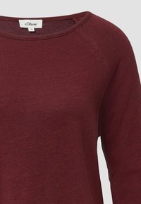 Burgundowa bluzka z długim rękawem o szerokim dekolcie, miękka w dotyku, z rękawami raglanowymi. Metka z napisem "s.Oliver". Gładki materiał z minimalnymi detalami.