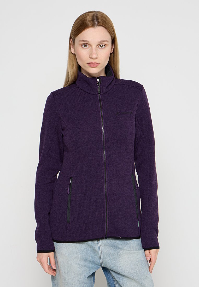 Lila Zip-Hoodie mit hohem Kragen, strukturiertem Stoff, zwei seitlichen Taschen und schwarzen Reißverschlüssen. Kombiniert mit hellen Jeans.