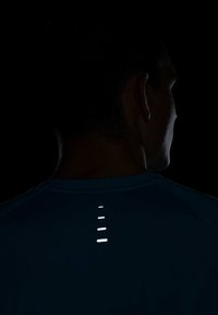 Camisa de mangas curtas azul escura com faixas verticais refletoras nas costas, destacando um design atlético e elegante.