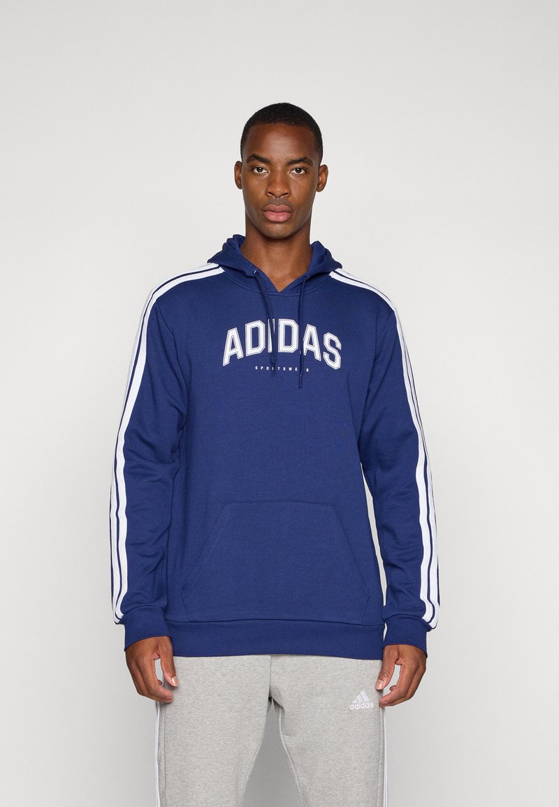 Marineblauwe hoodie met een voorzak, witte Adidas-tekst en drie witte strepen op de mouwen. Materiaal van katoenmix met een capuchon met trekkoord.