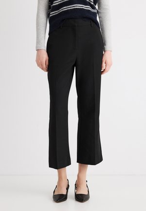 Mujer que lleva pantalones cortos anchos negros, tacones negros de tiras traseras, una camiseta de manga larga gris y un suéter sin mangas a rayas azul marino.