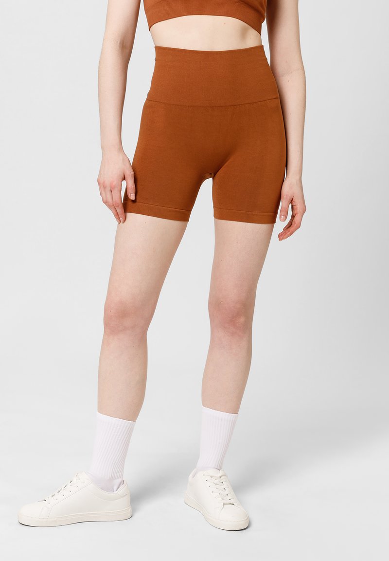 Bruine geribbelde sportshorts met een hoge taille en een gladde textuur, gecombineerd met witte sneakers en kniehoge witte sokken.