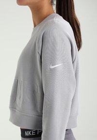 Grijze cropped sweatshirt van textuurstof, met een opvallend "JUST DO IT"-motief en een wit Nike-logo op de mouw.