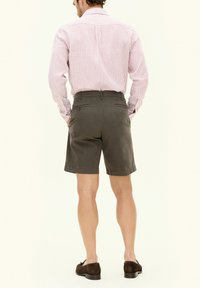 Pantaloni corti grigi da uomo con vestibilità su misura, dotati di passanti per la cintura e tasche laterali, abbinati a una camicia a maniche lunghe a strisce rosa e bianche.