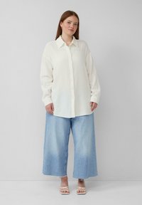 Witte overhemd met knopen en een textuur, gecombineerd met lichtblauwe wijde jeans en witte sandaaltjes met bandjes. Eenvoudig en ontspannen ontwerp.