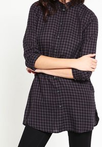Camicia a quadri nera e viola con colletto a punta, chiusura con bottoni sul davanti e maniche a tre quarti. Tessuto morbido con vestibilità comoda.