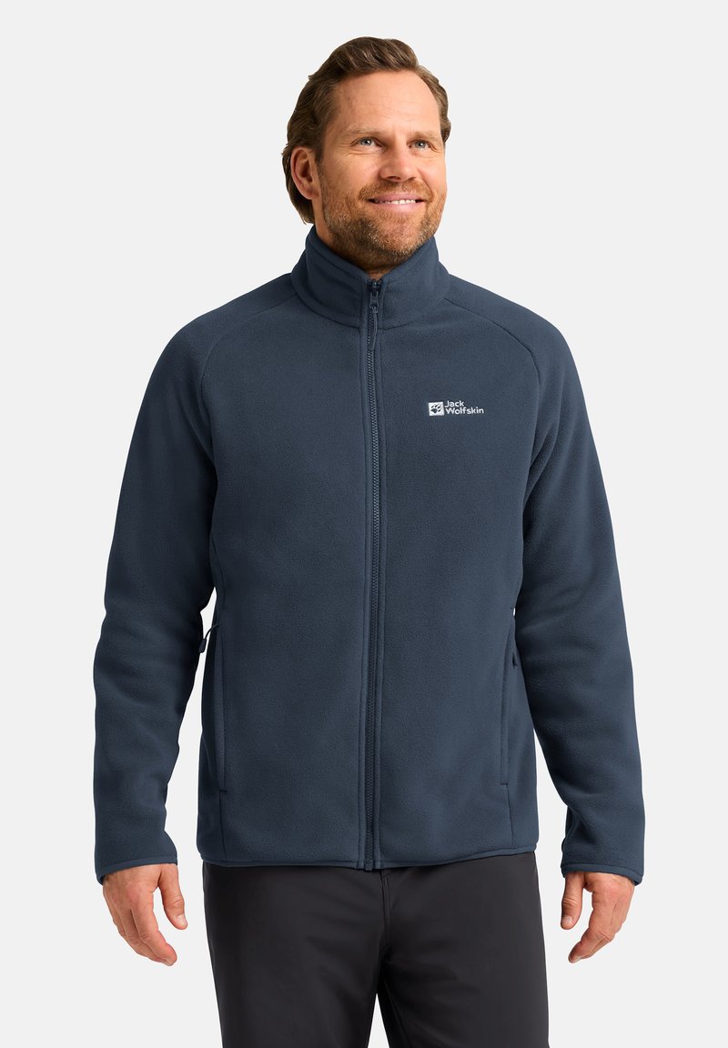 Giacca in pile blu navy con colletto alto e chiusura con zip. Presenta un logo sul lato sinistro del petto, tasche laterali e una texture morbida.