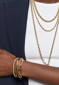 Gouden sieraden met meerdere kettingen in verschillende ontwerpen, een gelaagde look met gedraaide en gladde texturen, en een bijpassende armband.