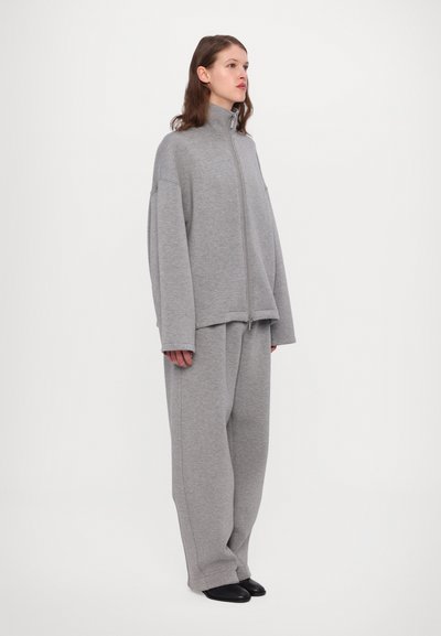 Hallgrey sweatshirt kõrge kraega ja täieliku tõmblukuga, koos laia ja vabade jalgade hallide pükstega. Pehme kangas, minimalistik disain ja sile tekstuur.