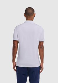 Biała koszulka polo z krótkim rękawem i klasycznym kołnierzykiem, o gładkiej fakturze i prostym obszyciu. W zestawieniu z granatowymi spodniami, widok od tyłu.