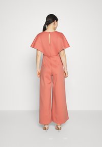 Ροζ φαρδύ ολόσωμο φόρεμα με μανίκια-cape, άνοιγμα στην πλάτη και λεία υφή. Απλός σχεδιασμός με κομμένο μπούστο και χαλαρή εφαρμογή.