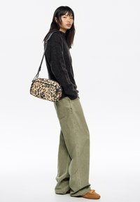 Bolso bandolera con estampado de leopardo de forma estructurada, material de tela y correa de hombro extraíble, combinado con pantalones anchos verdes sueltos.
