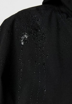 Juoda medžiaga su vandens lašeliais, kurie susitelkia į burbuliukus ir nuteka žemyn paviršiumi, pabrėžiant jos vandeniui atsparias savybes.