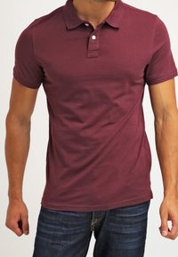 Polo shirt bordeaux in cotone, con colletto classico, placca con tre bottoni e maniche corte. Tessuto liscio, design aderente.