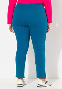Teal leggings med en åtsittande design, tillverkade av mjukt material, med en slät textur och en elastisk midja. Bärs med flerfärgade sneakers.