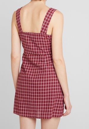 Robe à carreaux rouges avec larges bretelles, corsage ajusté et jupe évasée. Le tissu semble texturé avec un motif à carreaux.