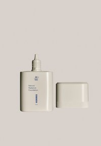 Natural Radiance Foundation i en cremefarvet, rektangulær flaske med en dysedæksel. Inkluderer et lille, struktureret rundt låg.