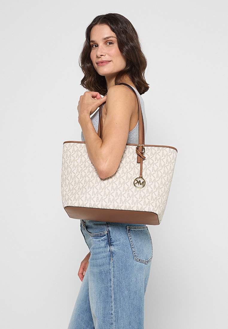 Sac en toile crème avec motif monogramme MK. Base et accents en cuir marron, quincaillerie en or. Anses de longueur épaule.