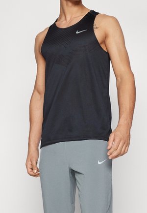 Man wearing black sleeveless athletic shirt and light gray fitted sports pants with Nike logos on both garments.