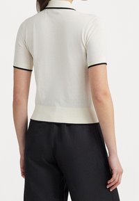 Polo classique à manches courtes couleur crème avec bordure noire, doté d'une coupe ajustée et d'une texture côtelée. Vue arrière montrant une silhouette épurée.