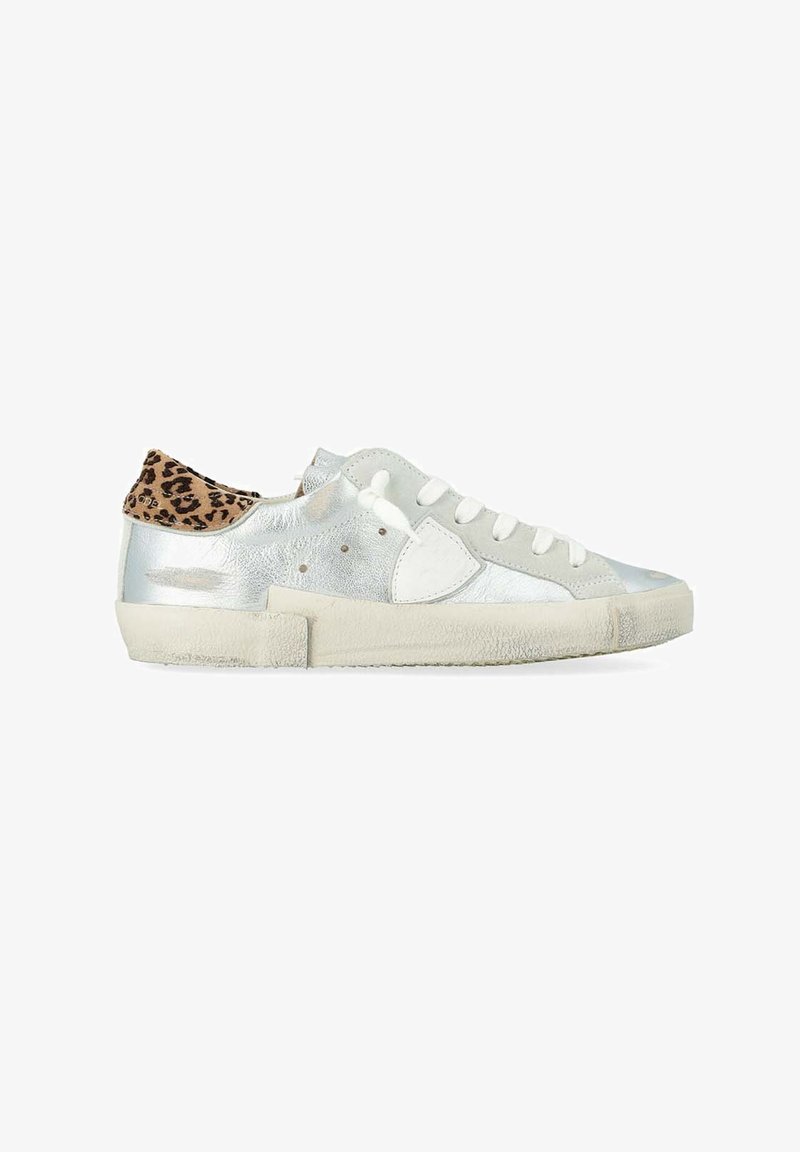 Zapatilla baja con cuerpo plateado metálico, cordones blancos, suela beige y lengüeta del talón con estampado de leopardo, vista lateral sobre fondo blanco.