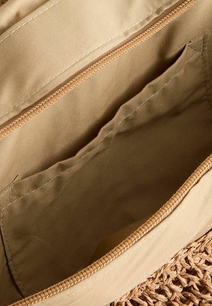 Interno di una borsa di stoffa beige con chiusura a zip, due tasche interne e un accento intrecciato sul bordo esterno. Texture liscia e opaca.