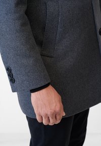 Grijze wollen overjas met een getailleerde pasvorm, drie zwarte knopen op de manchetten en een zijzak. Glad textuur en slank ontwerp.