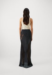 Jupe maxi noire avec des panneaux en dentelle transparente, dotée d'un design à fente haute. Le tissu est léger avec une texture lisse et un aspect superposé.
